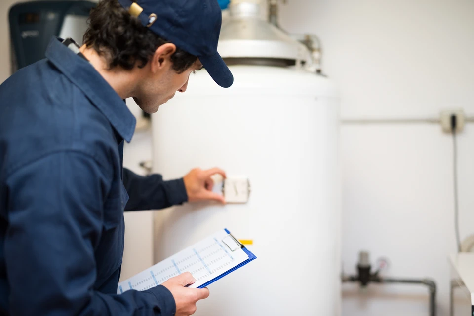 Technicien en uniforme bleu travaillant dans une cuisine professionnelle blanche, tenant un presse-papiers avec formulaire d'inspection, effectuant un contrôle qualité ou maintenance d'équipements de restauration