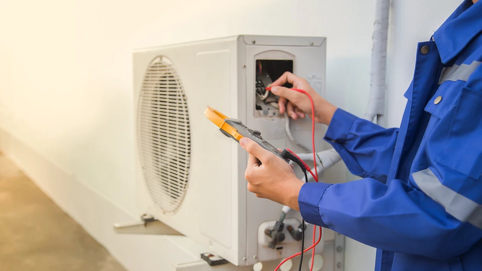 Technicien en uniforme bleu effectuant la maintenance d'une unité de climatisation extérieure blanche