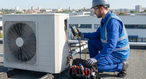 Photographie d'un frigoriste professionnel en uniforme (combinaison de travail bleu ou grise avec logo de l'entreprise) effectuant une maintenance sur une unité de climatisation ou de froid industriel. Le technicien doit être photographié en action, contrôlant ou vérifiant des connexions de fluides frigorigènes sur un système installé (par exemple une unité extérieure de climatisation ou une installation de chambre froide). L'arrière-plan doit montrer un environnement professionnel (bâtiment commercial, installation industrielle ou résidentielle). L'image doit transmettre la confiance, la compétence et le professionnalisme, illustrant le savoir-faire technique de l'entreprise en matière de froid et climatisation. Cadrage net et professionnel, éclairage naturel ou semi-professionnel, sans texte ni logo visible.