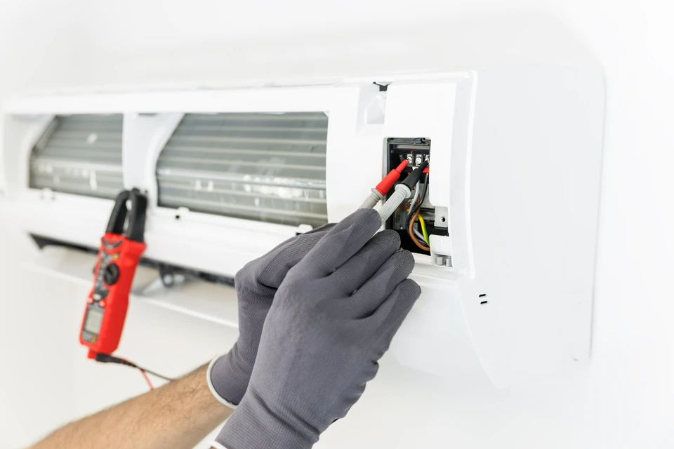 Technicien en tenue de travail bleue effectuant maintenance sur système de climatisation résidentiel
